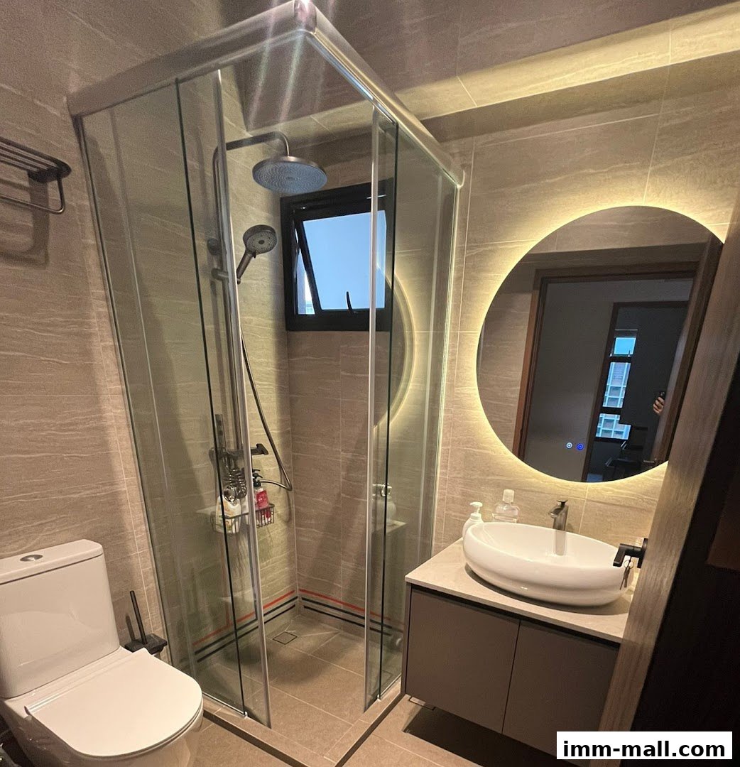 A modern bathroom featuring a glass shower enclosure, toilet, and vanity with a backlit mirror.