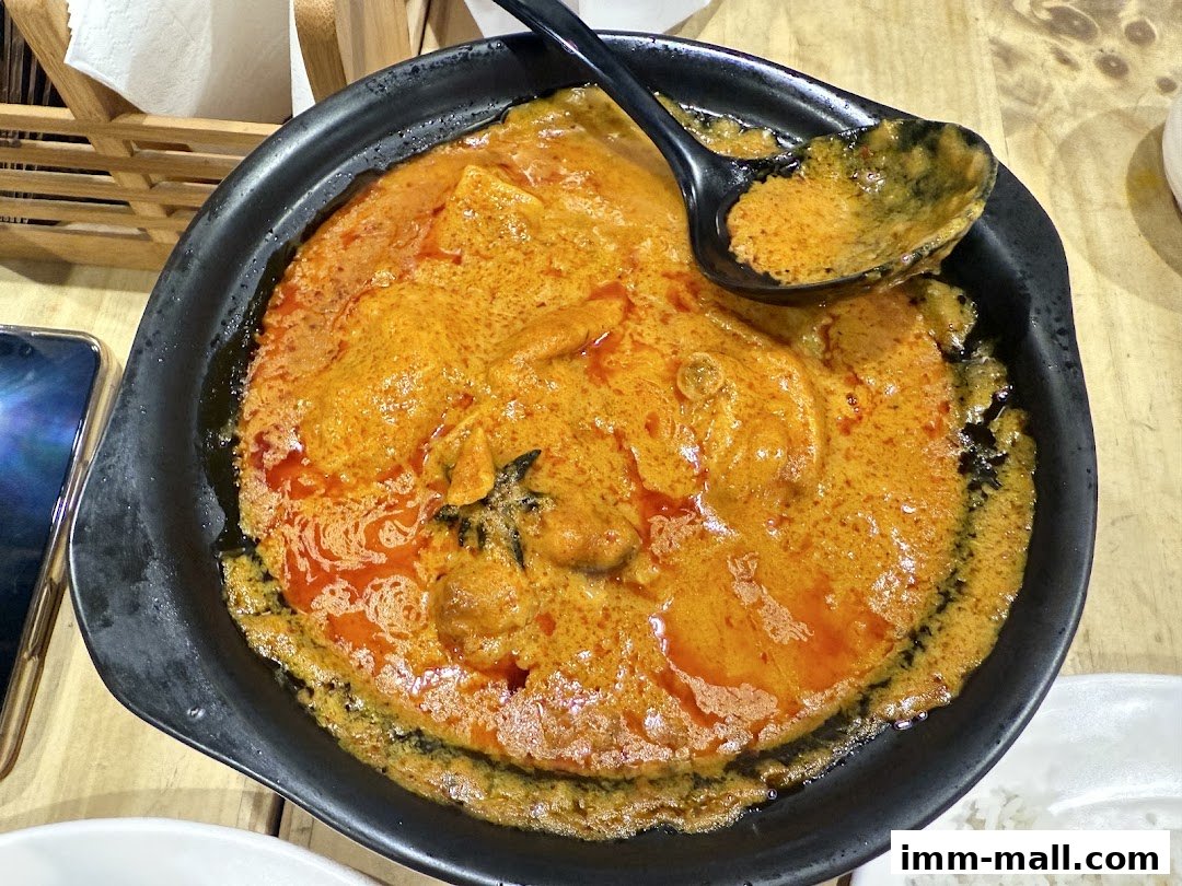 A close-up shot of a rich, creamy curry dish served in a black bowl with a spoon.