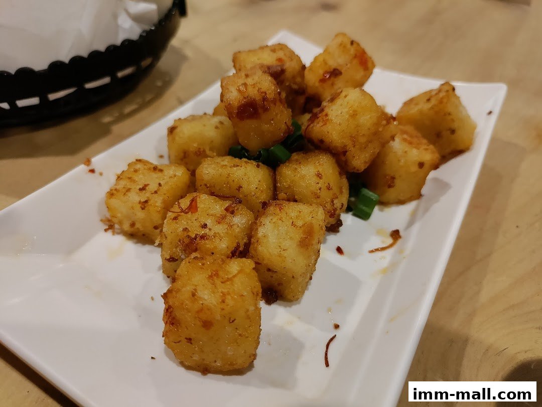 A plate of crispy fried tater tots seasoned with chili flakes and garnished with green onions.