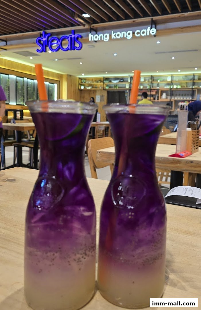 Two purple drinks with orange straws sit on a wooden table at Streats Hong Kong Cafe.