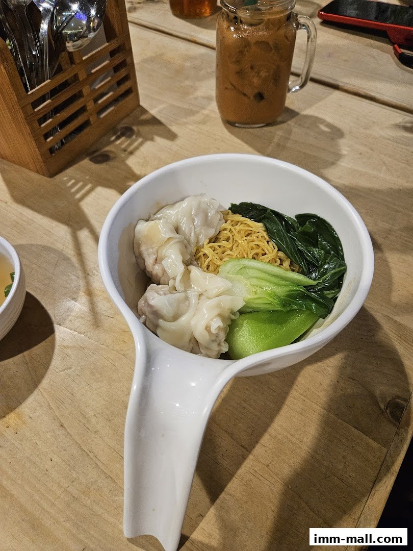 A bowl of wonton noodles with bok choy and a refreshing iced drink.