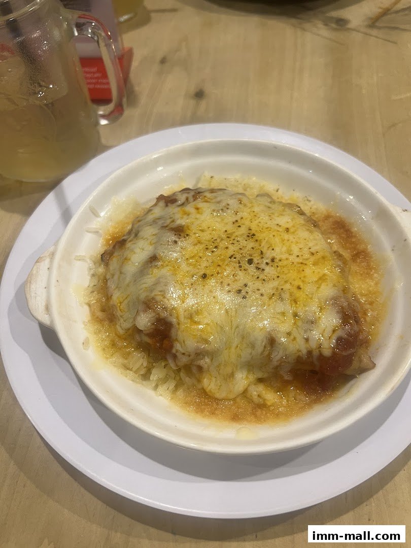 A close-up of a cheesy baked dish with rice and a glass of iced tea.