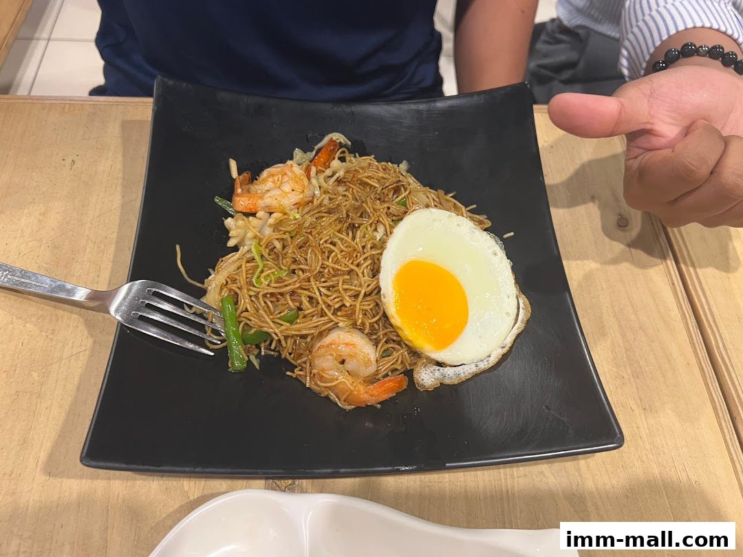 A plate of stir-fried noodles with shrimp and a fried egg, served with a fork.