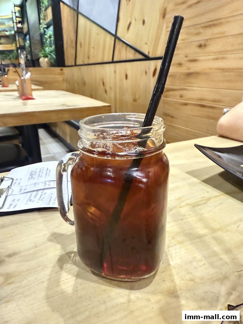 A glass jar filled with iced tea and a straw sits on a wooden table.