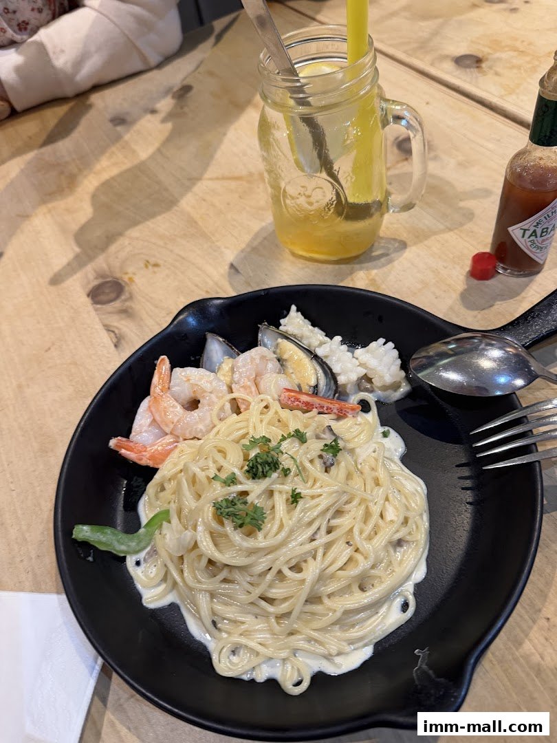A plate of creamy seafood pasta with shrimp and mussels, served with a drink.