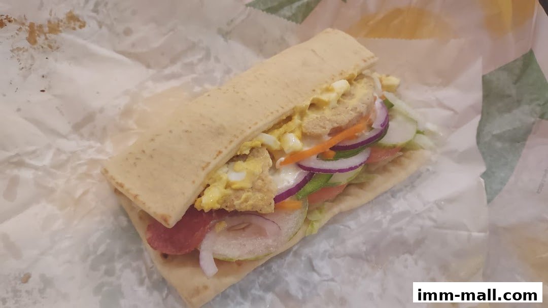 A Subway sandwich with various fresh ingredients and meat, wrapped in paper.