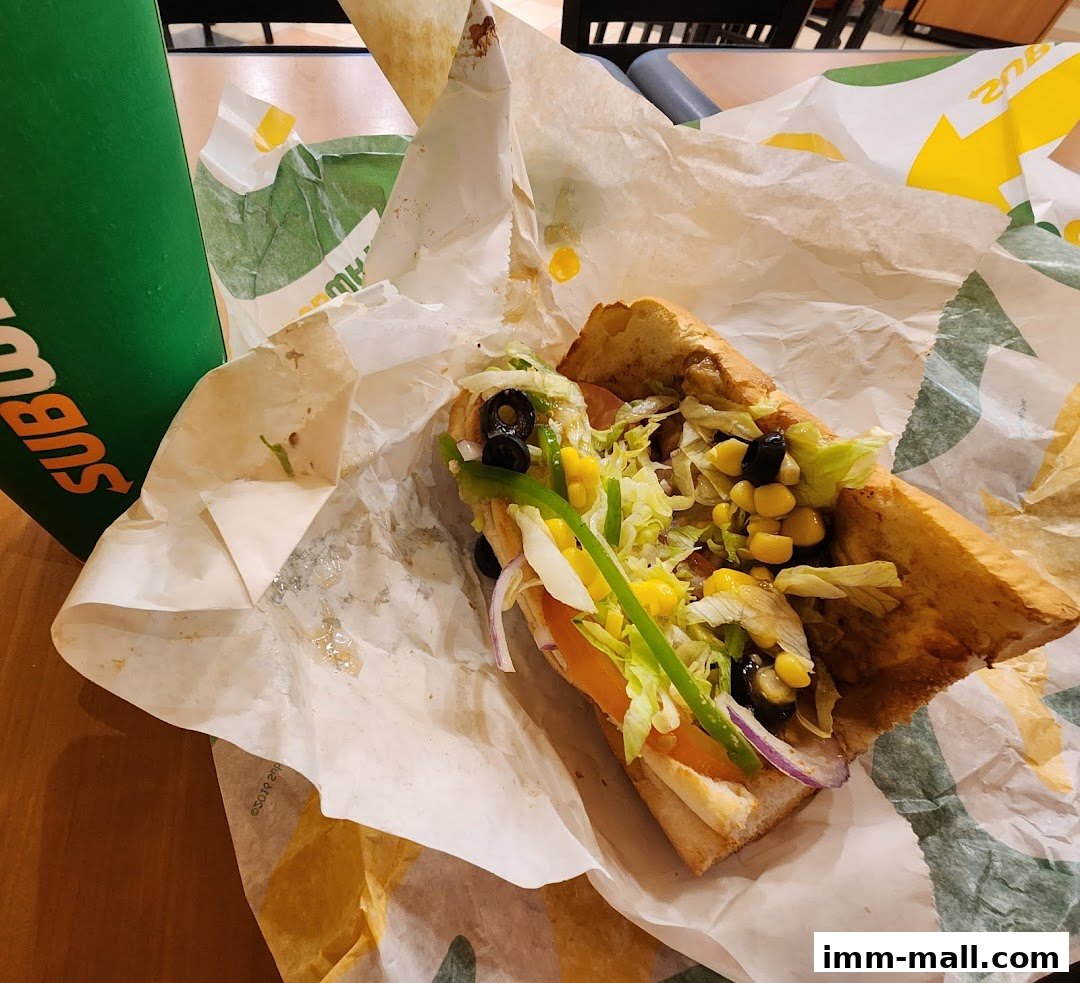 A Subway sandwich with fresh vegetables and a green drink on a table.