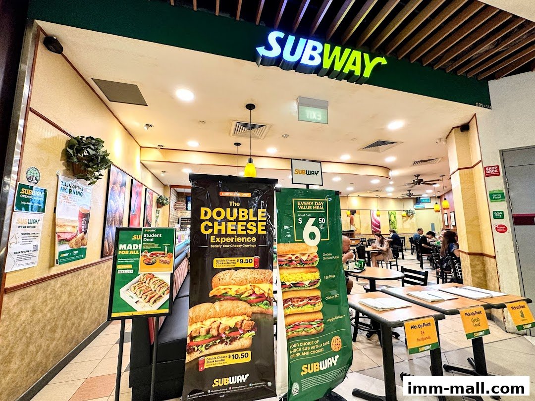 The exterior of a Subway restaurant with promotional banners and seating visible inside.