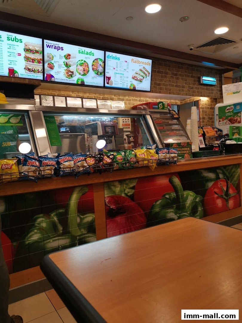 A Subway restaurant counter with digital menus displaying subs, wraps, salads, drinks, and flatbreads.