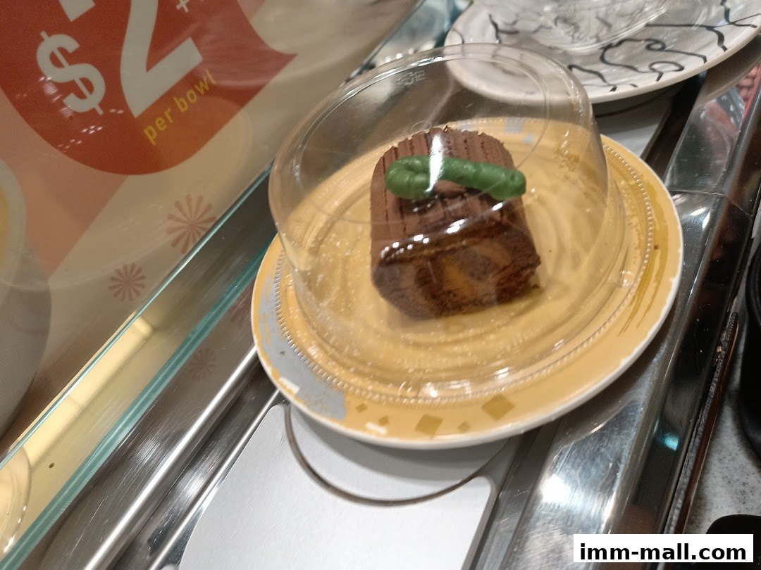 A chocolate dessert on a plate with a clear dome cover on a conveyor belt.