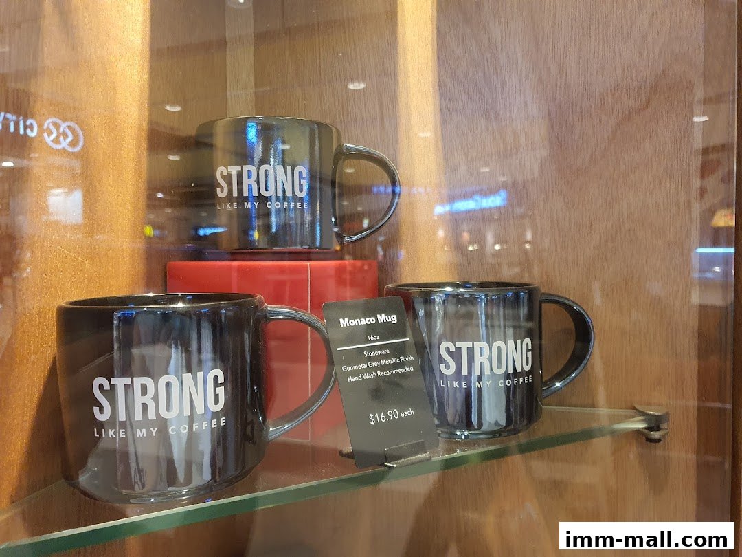 Three black mugs with "STRONG LIKE MY COFFEE" text displayed in a shop window.