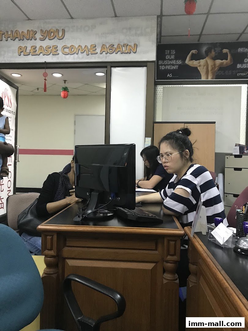 People working at desks in an office with a "Thank You, Please Come Again" sign.