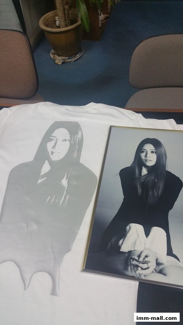 A white t-shirt with a grey portrait print next to a framed portrait of a woman.