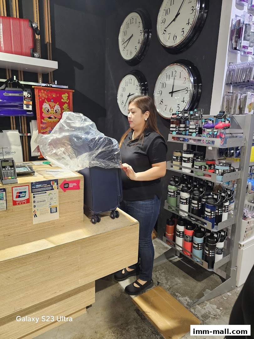 A woman stands near a checkout counter with luggage and travel accessories in a store.