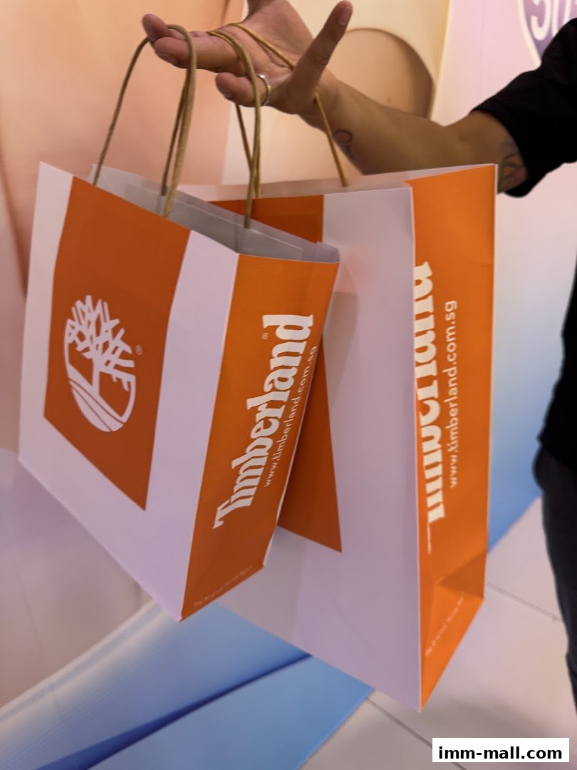 A person holds two Timberland shopping bags with the brand logo and website.