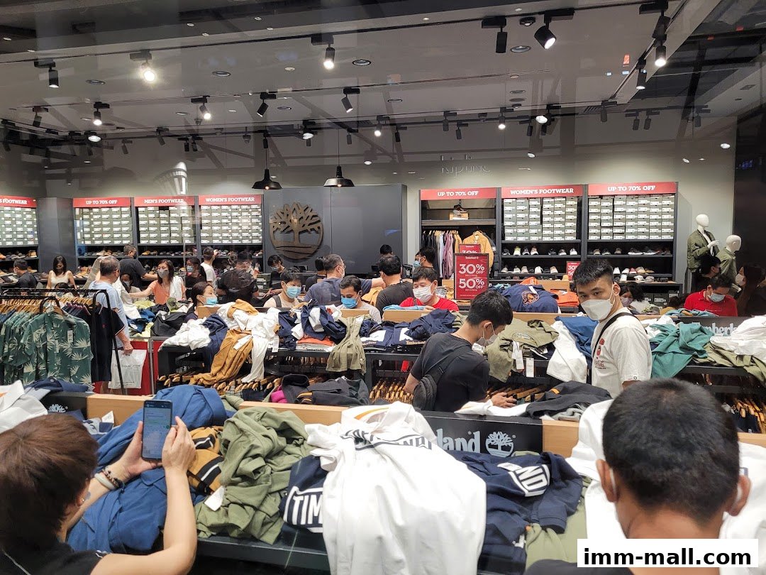 Shoppers browse clothing and footwear in a busy Timberland store with sale signs.