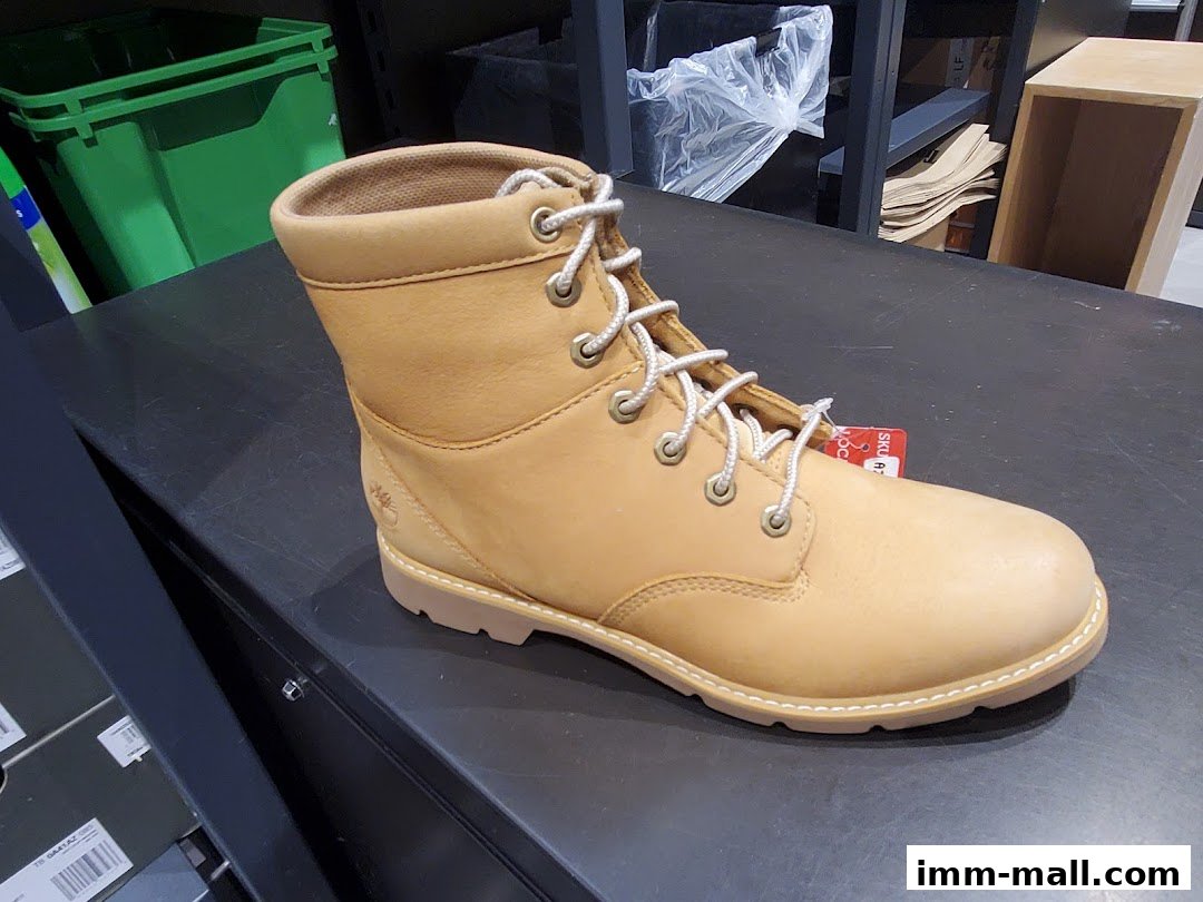 A close-up view of a tan Timberland boot with white laces on a dark surface.