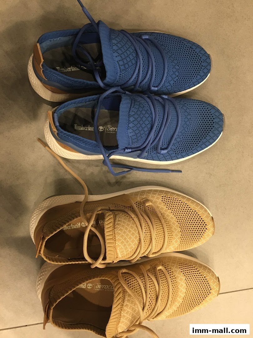 Two pairs of Timberland sneakers, one blue and one tan, displayed on a tiled floor.