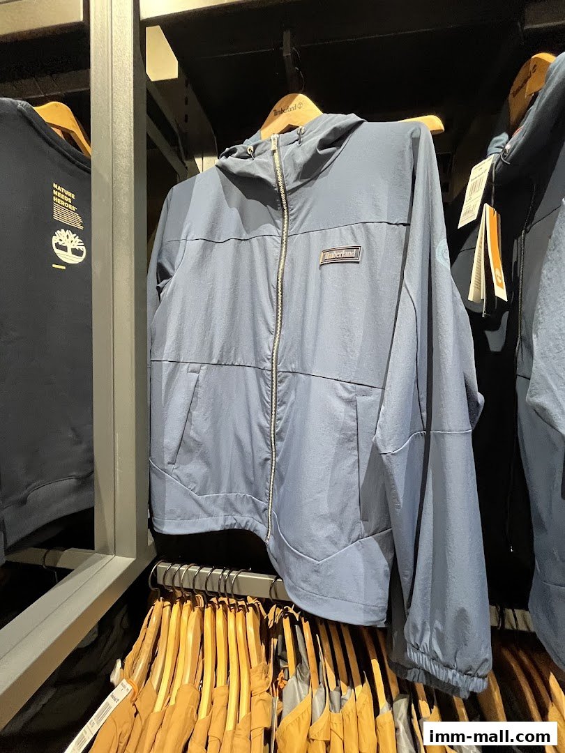 A blue Timberland jacket with a hood hangs on a hanger, with other clothing visible.