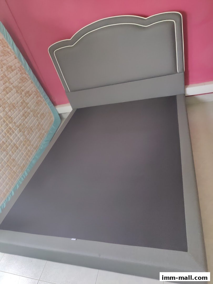 A modern grey bed frame with a decorative headboard and a mattress beside it.