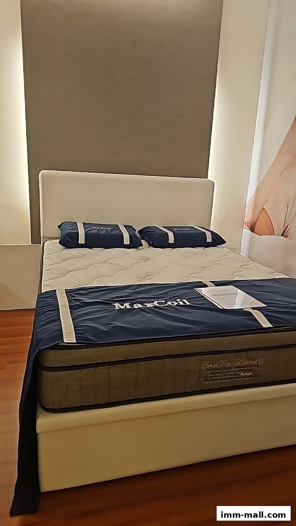 A display of a MaxCoil mattress with pillows and a blue cover in a retail setting.