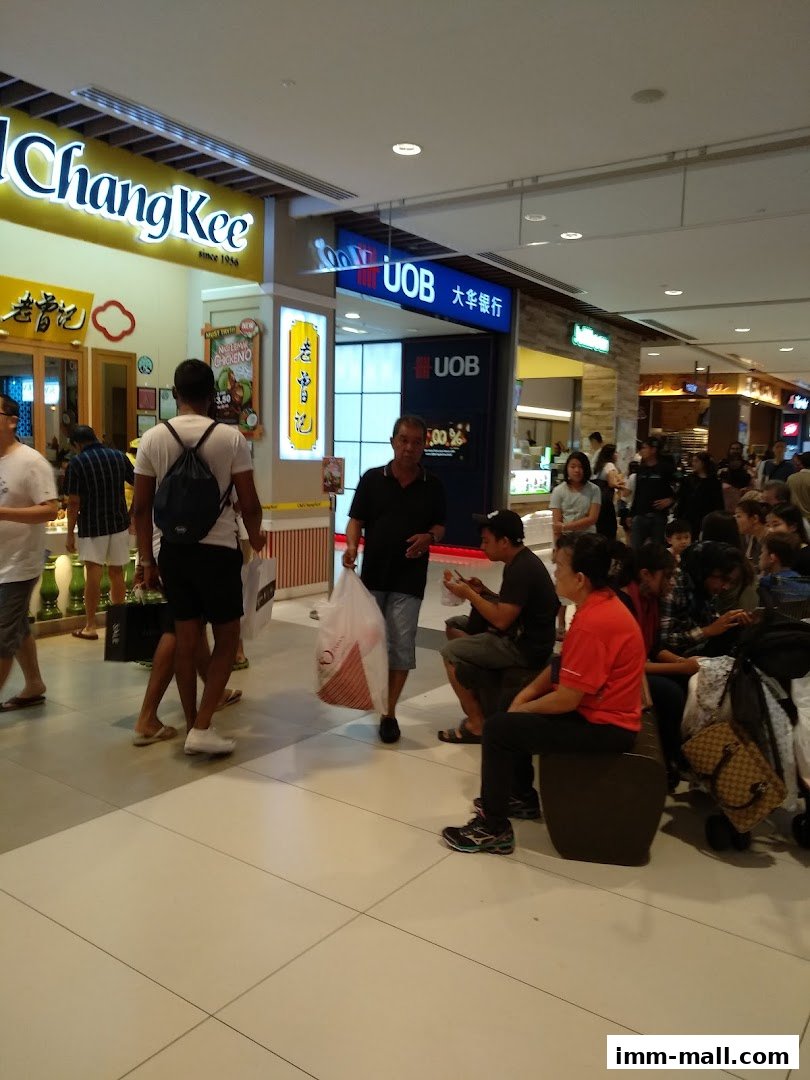 People walking and sitting in a mall hallway with shops like Chang Kee and UOB visible.