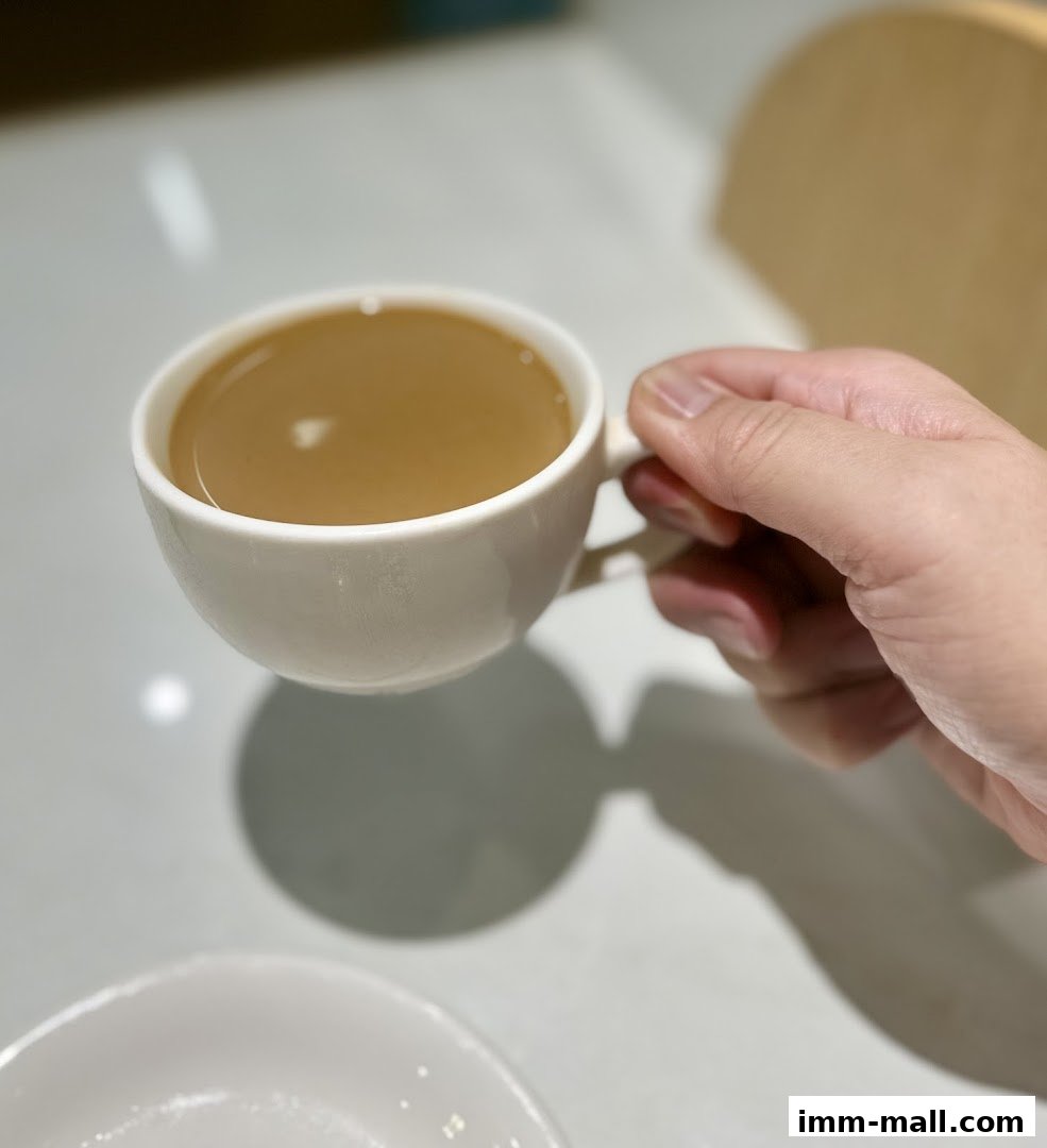 A hand holds a white cup filled with a light brown beverage, casting a shadow.