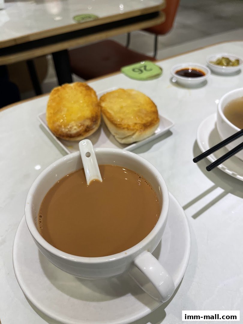 A cup of Hong Kong-style milk tea and two baked buns with butter on a table.
