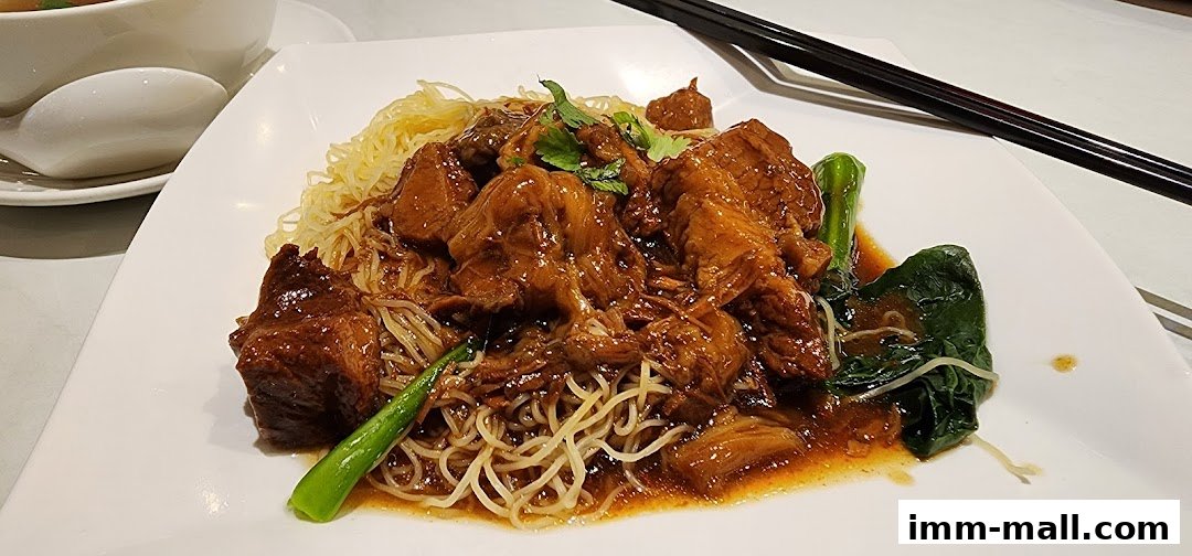 A plate of braised beef noodles with greens and chopsticks.