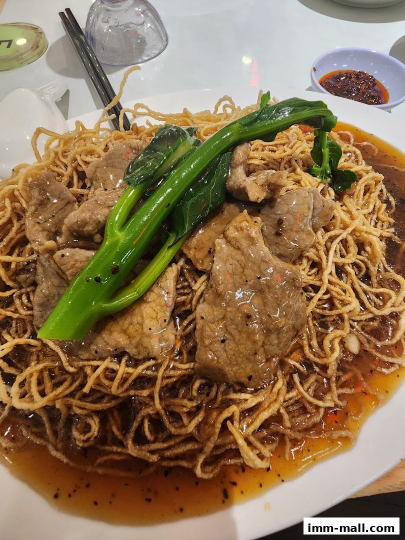 A plate of crispy noodles topped with beef and green vegetables in a savory sauce.