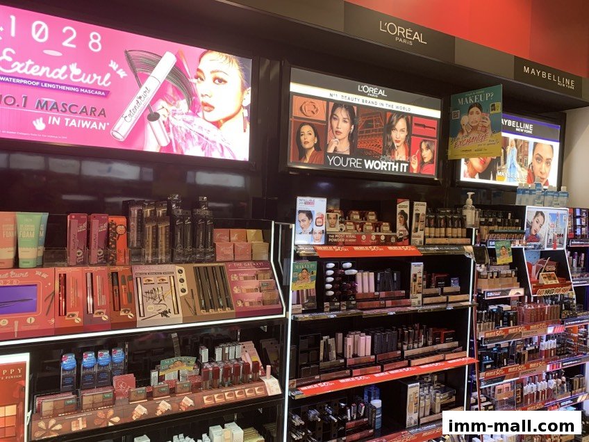 A wide selection of makeup and beauty products displayed on shelves, with brand advertisements overhead.