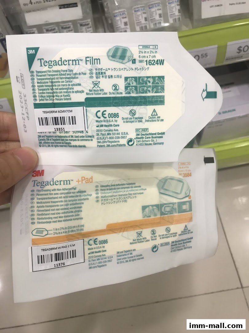 A hand holds two packages of 3M Tegaderm medical dressings, showing product details.