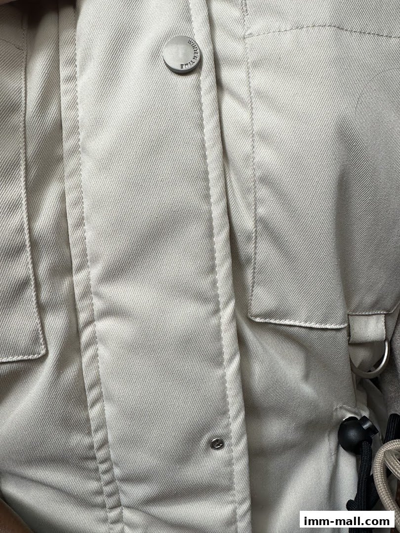Close-up of a light-colored jacket with prominent stitching and metal buttons.