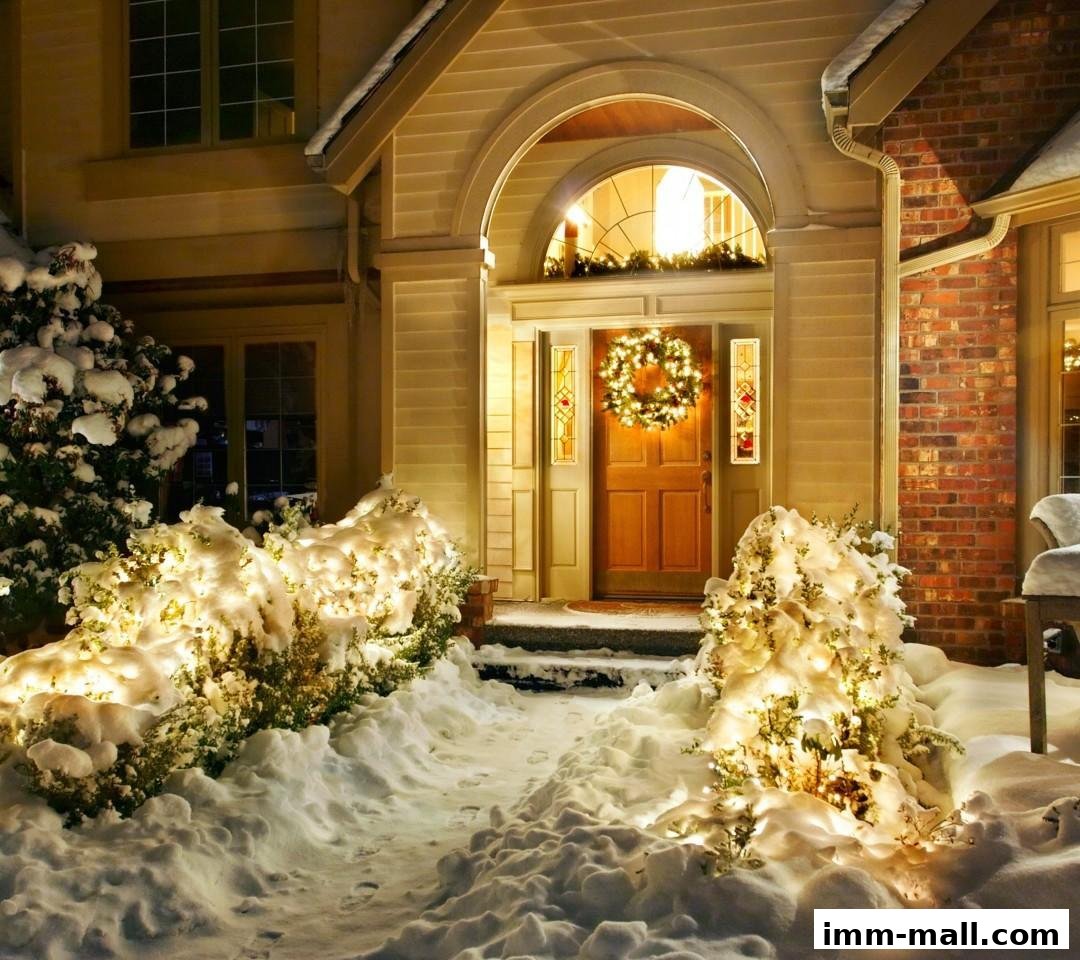 A snow-covered house entrance at night, decorated with a wreath and lights.