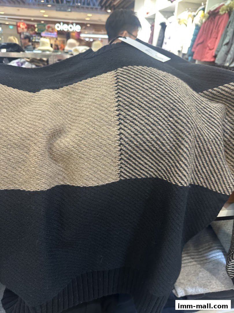 A person holds up a black and beige checkered sweater in a clothing store.