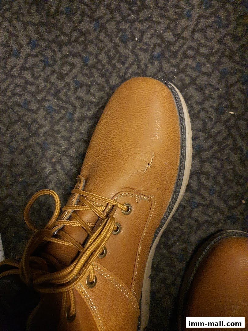 A close-up view of a tan leather boot with yellow laces on a dark carpet.
