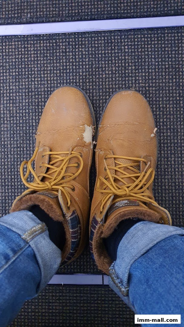 A pair of worn tan boots with yellow laces and plaid lining, paired with cuffed jeans.