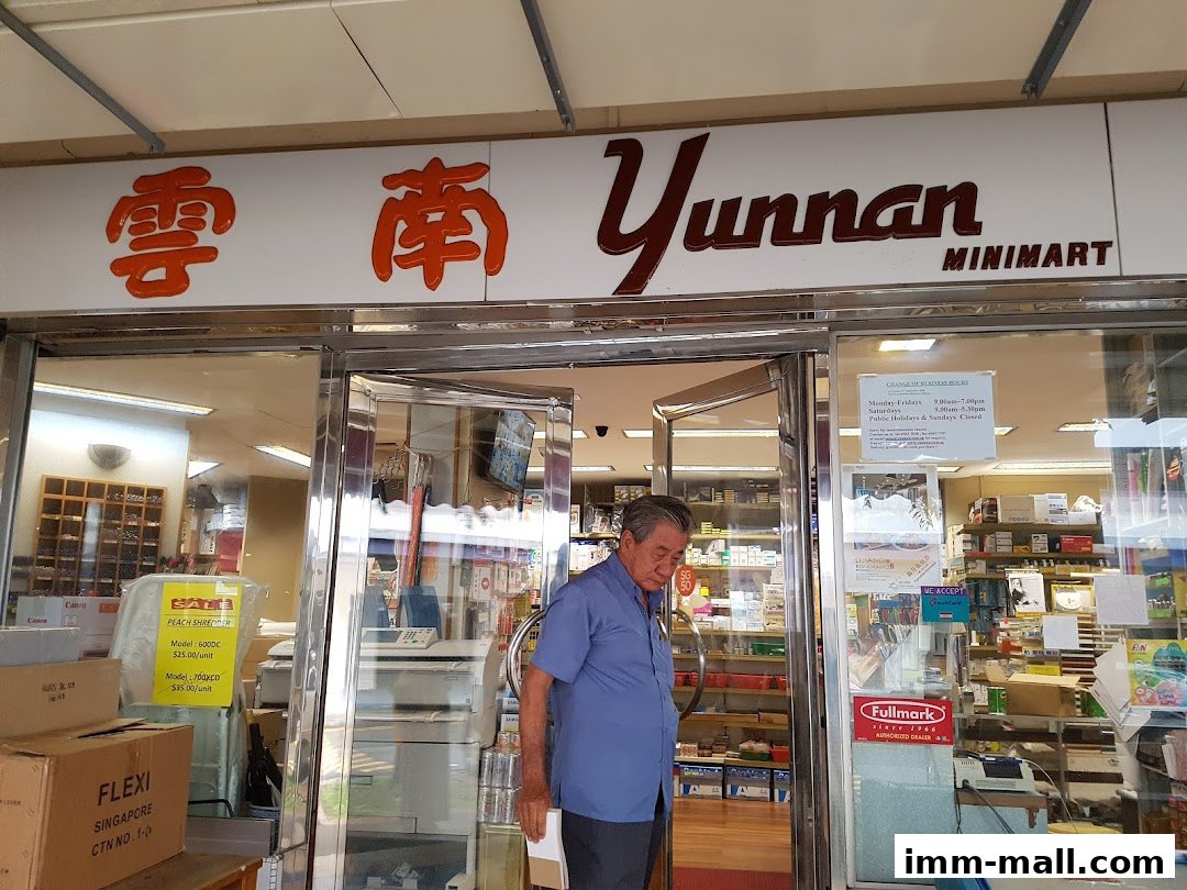 A man stands at the entrance of Yunnan Minimart, a shop with a prominent sign and shelves stocked with goods.
